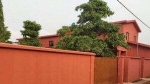 A red building with a gated entrance and a pathway leading to it. - Lagoon Residence Appt Bioguera (Porto-Novo)