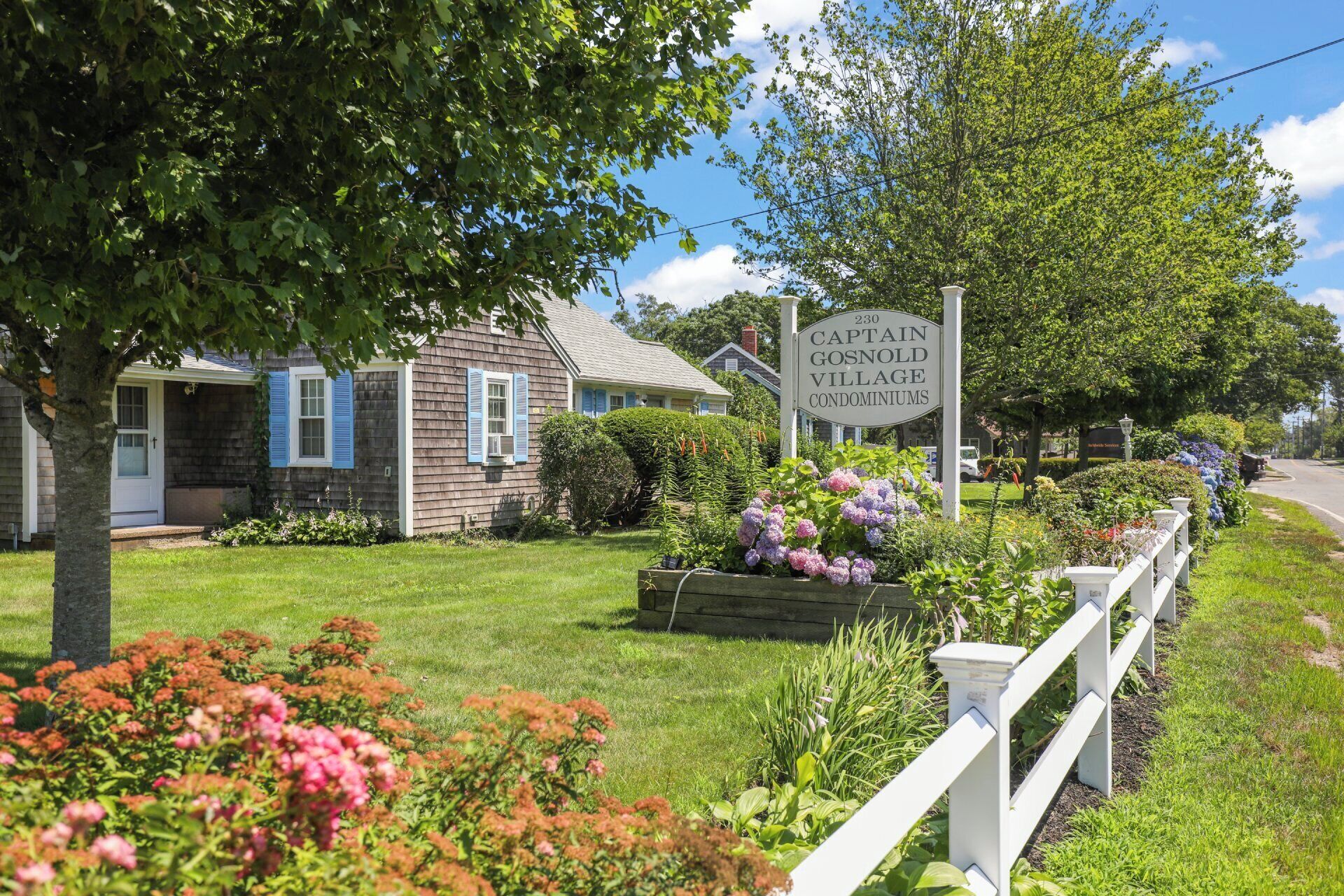 A sign for Captal Gosnold Village Condominiums, surrounded by well-maintained lawns and a white picket fence.