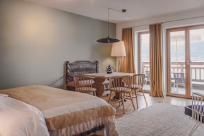 Une chambre d’hôtel avec un lit, une table et des chaises, une lampe, et une vue sur l’extérieur grâce à de grandes fenêtres.