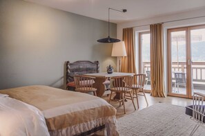 Une chambre d’hôtel avec un lit, une table et des chaises, une lampe, et une vue sur l’extérieur grâce à une porte-fenêtre coulissante.