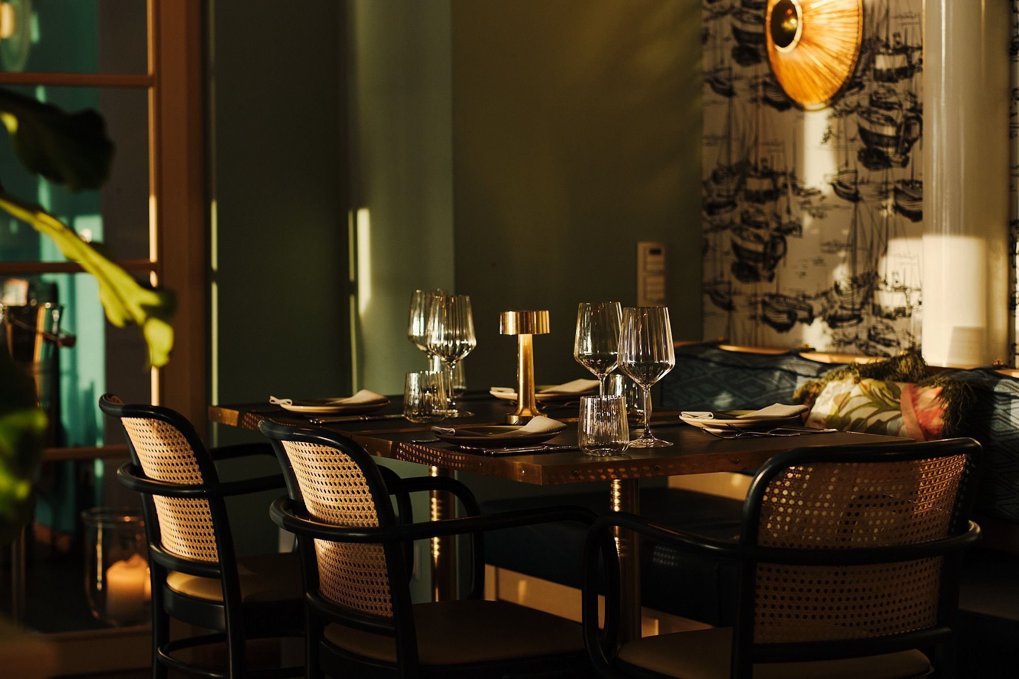 A dining table set for six with chairs, a lamp, and a patterned wallpaper.