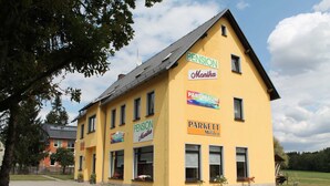 Un bâtiment jaune orné de plusieurs enseignes, dont « Pension Manika » et « Parkett Milster ».