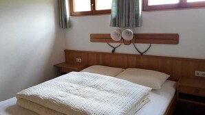 Un dormitorio con cabecera de madera, dos mesitas de noche, una cama con manta blanca y un ventanal con cortinas.