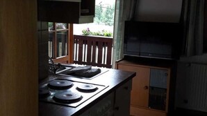 Una cocina con estufa, armarios, un ventanal con vista a la vegetación y un televisor.