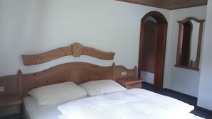 Een enkel bed met een houten hoofdbord, een nachtkastje en een spiegel aan de muur.