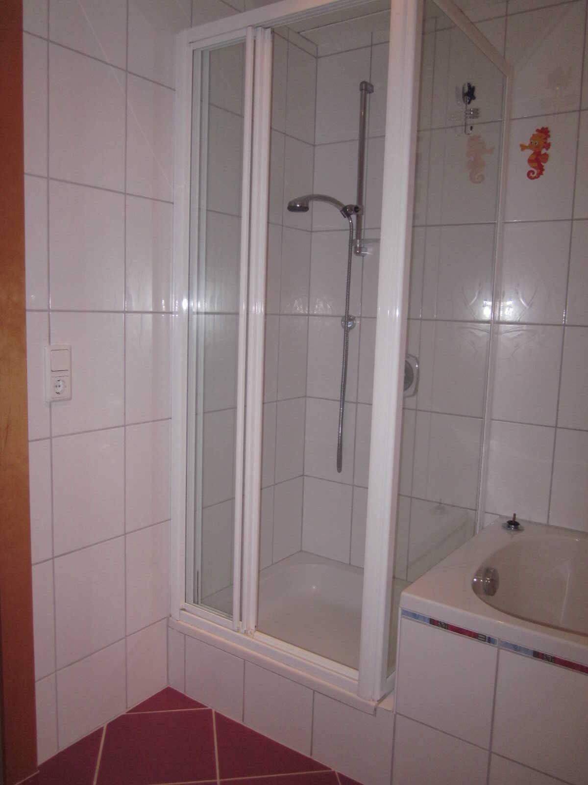 Une douche avec une porte en verre, un mur carrelé et un lavabo avec un miroir.