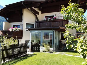 Un chalet doté d’un balcon en bois, d’une entrée avec porte vitrée et d’un jardin clôturé.