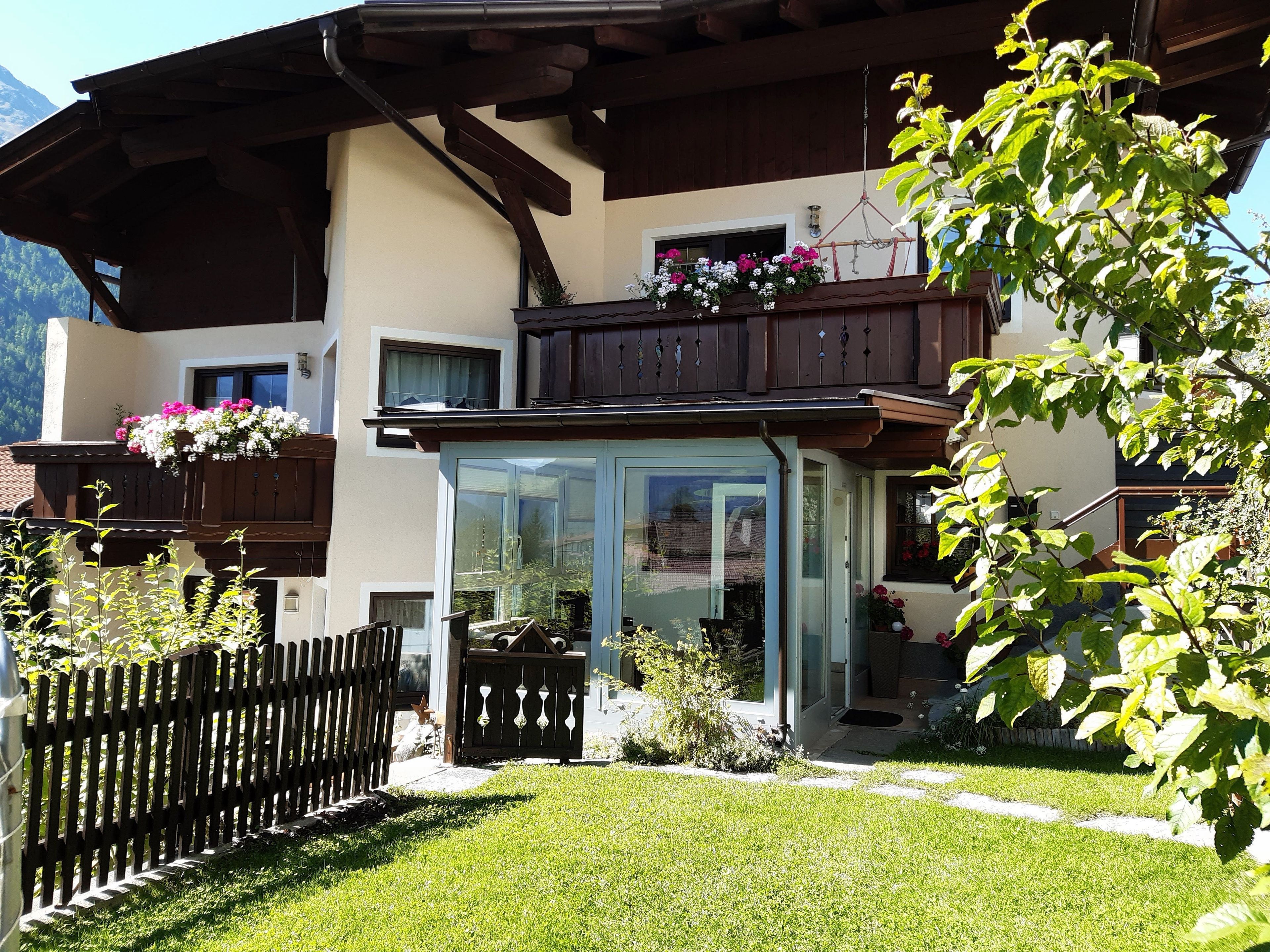 Een chalet met een houten balkon, een glazen deur en een omheinde tuin.