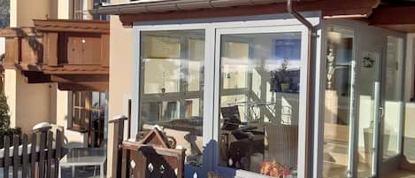 Un chalet doté d’une entrée en verre, d’une terrasse en bois et d’un terrain enneigé.