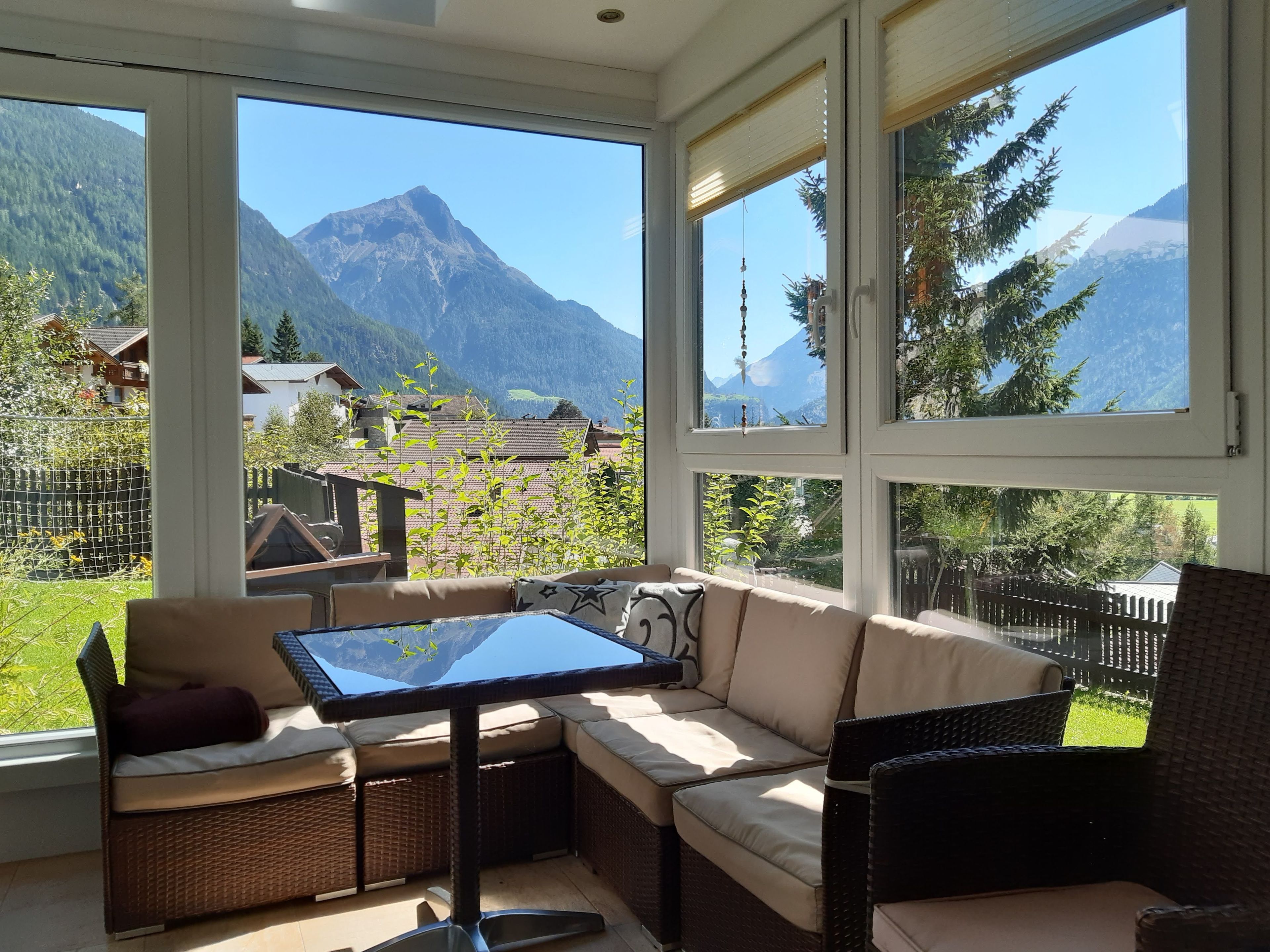 Ein Zimmer mit großen Fenstern, einer Couch, einem Tisch und einem Sessel.