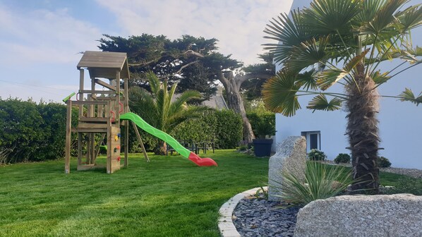 A wooden play structure with a slide in a well-maintained garden.
