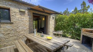 Fachada de piedra con una terraza de madera, zona de barbacoa y mesa de patio con un frutero.