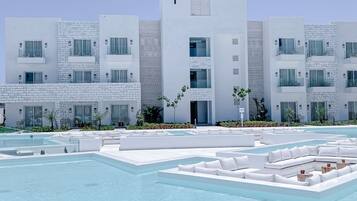 Un hotel moderno con zona de piscina, con edificios blancos con balcones y un cielo azul despejado.