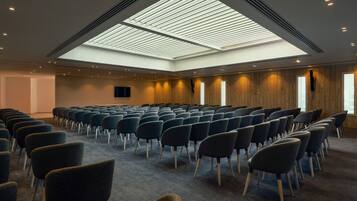 A conference room with rows of chairs, a skylight ceiling, and wooden panel walls.