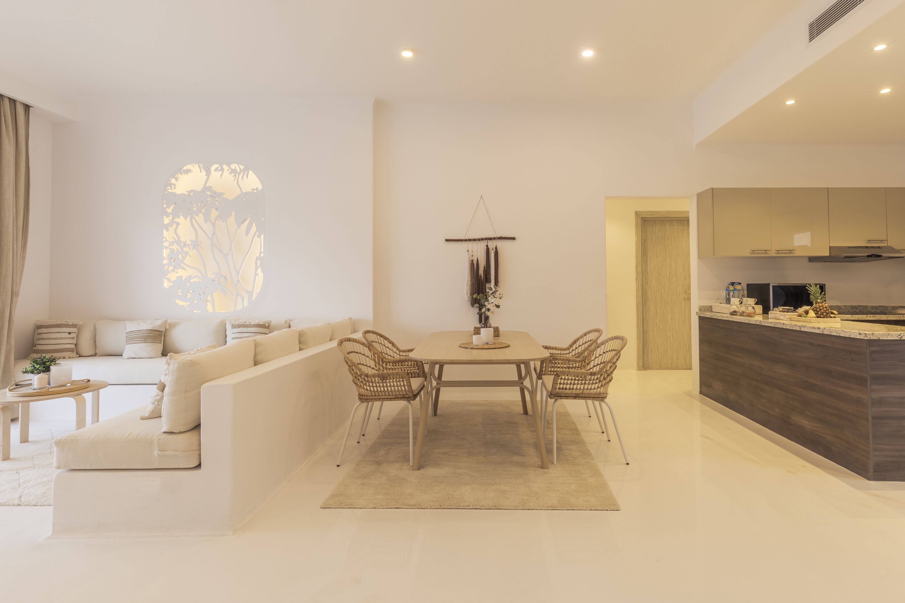 A modern living room with a sofa, dining table, and chairs. There is a kitchen area with cabinets and a countertop.