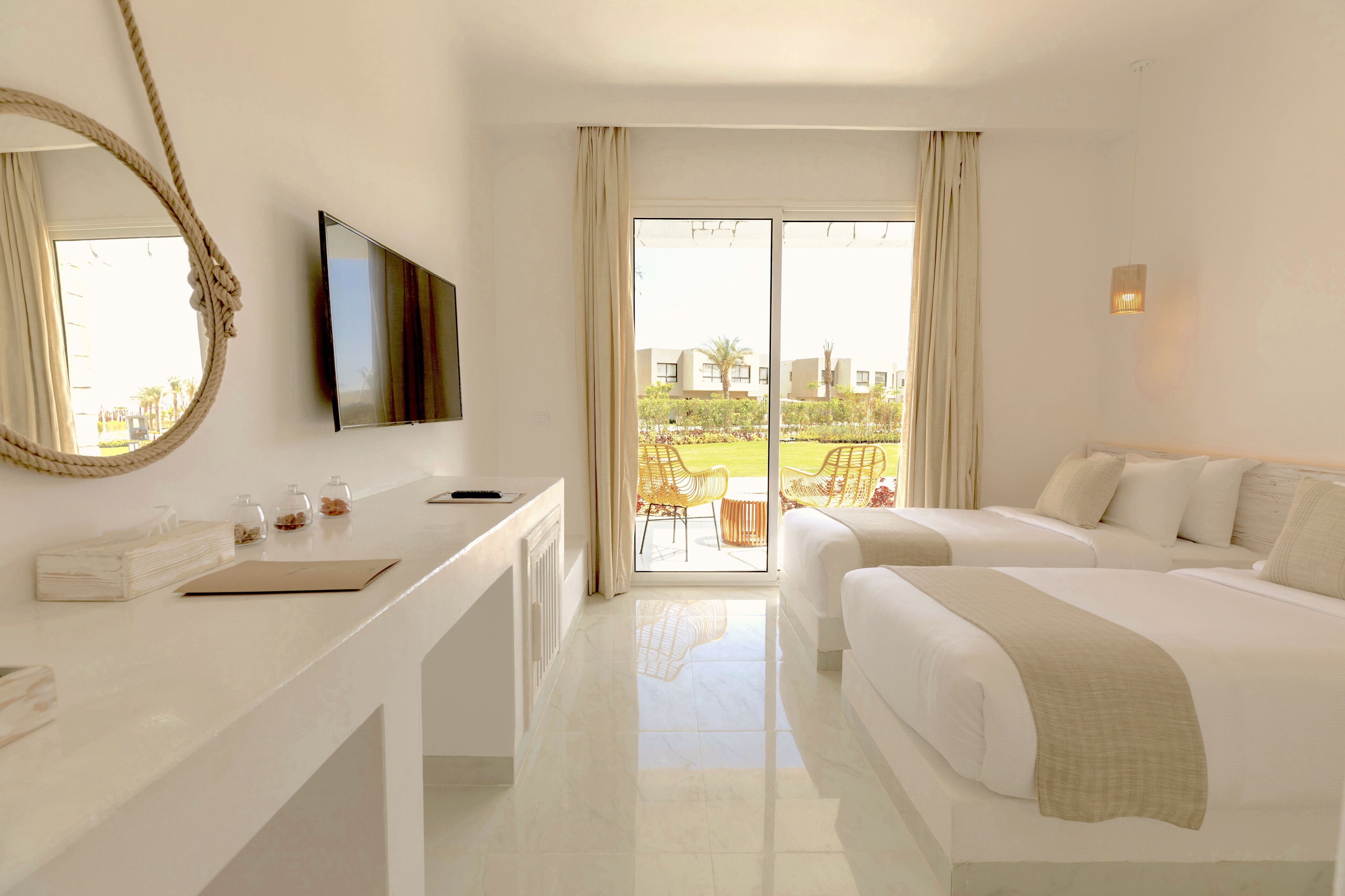 Habitación de hotel con un ventanal grande, un televisor de pantalla plana, un escritorio con libreta y gafas, dos camas y vistas al exterior.