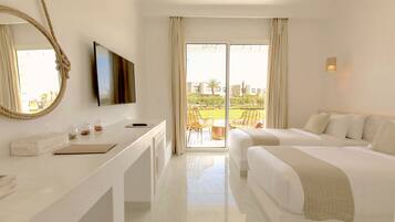Habitación de hotel con un ventanal grande, un televisor de pantalla plana, un escritorio con libreta y gafas, dos camas y vistas al exterior.