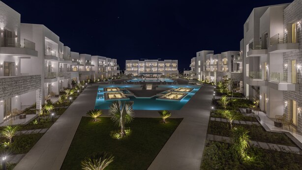 A modern hotel with multiple white buildings, a central swimming pool, and well-lit pathways. - Tanoak Resort (Ataqah)