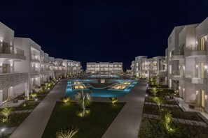 Un hôtel moderne composé de plusieurs bâtiments blancs, doté d’une piscine centrale et de chemins bien éclairés.