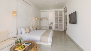 A modern hotel room with a large bed, a round coffee table with fruits, a sofa, a TV, and a wardrobe. - Tanoak Resort (Ataqah)