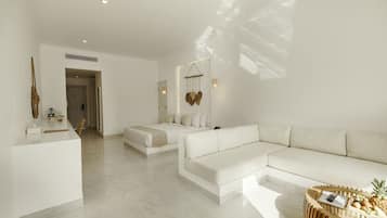 Une chambre d’hôtel moderne aux couleurs claires, comprenant un lit, un canapé, une table basse et un bureau.