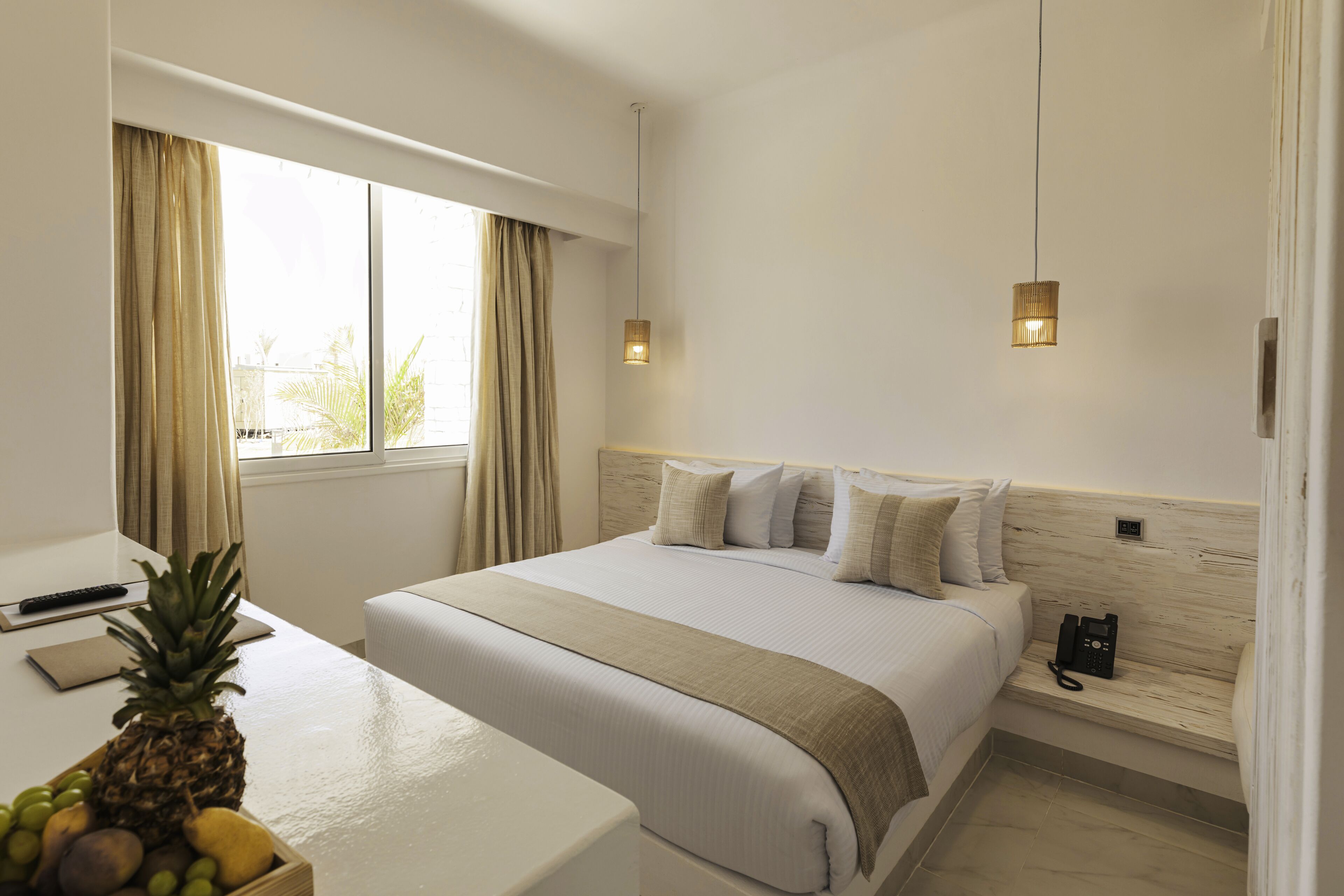 A hotel room with a bed, bedside table, and a fruit bowl.