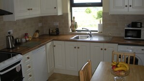 Una cucina con mobili bianchi, un piano di lavoro in legno, un lavello, un forno a microonde e un tavolo da pranzo con una ciotola di frutta.