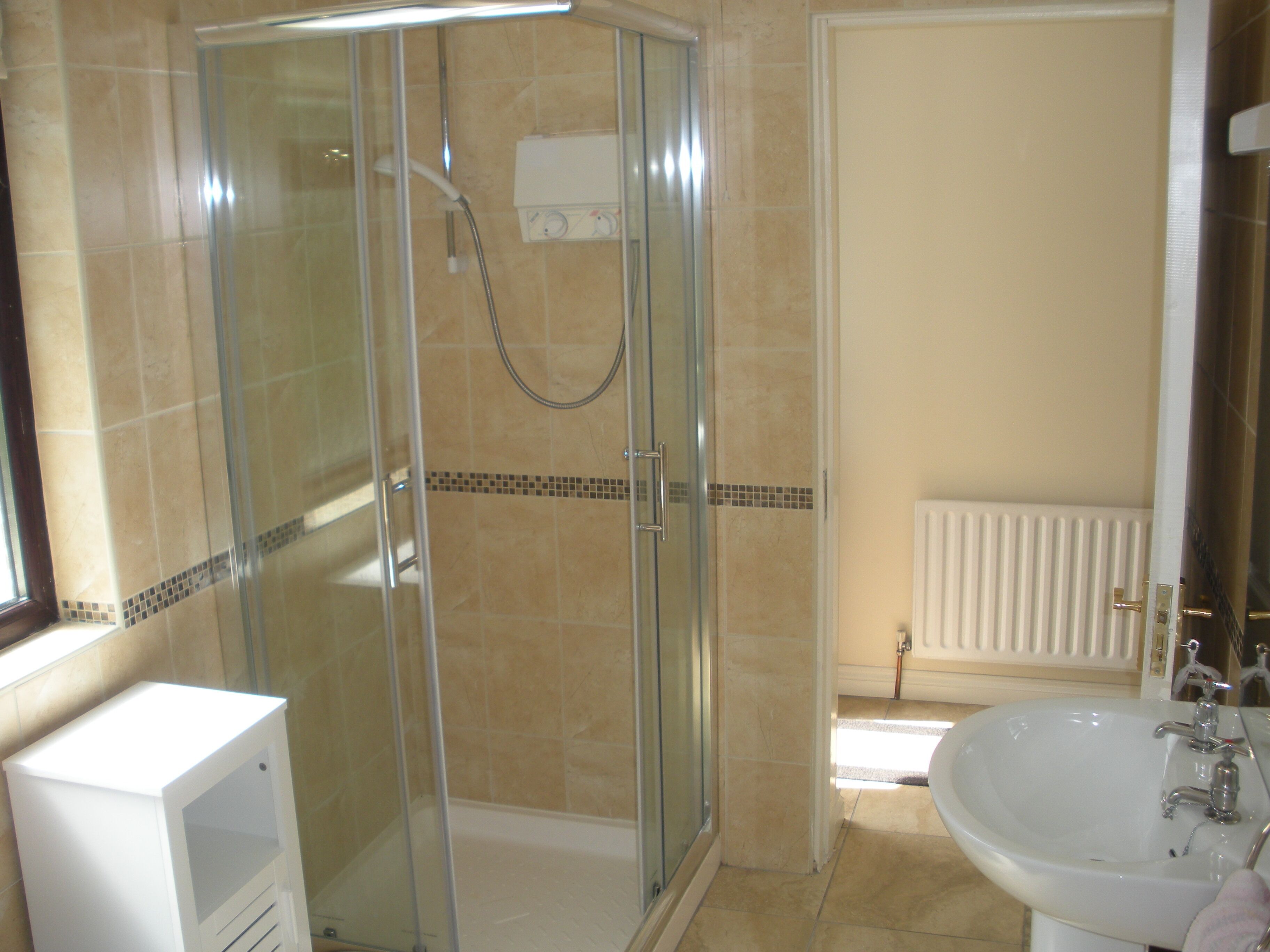 Un baño con ducha acristalada, lavabo blanco y radiador.