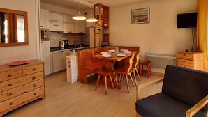 A compact kitchen with wooden cabinets, a dining table set for four, and a television on the wall. - Beautiful 3-room apartment for 7 with balcony, Montgenèvre (Montgenèvre)