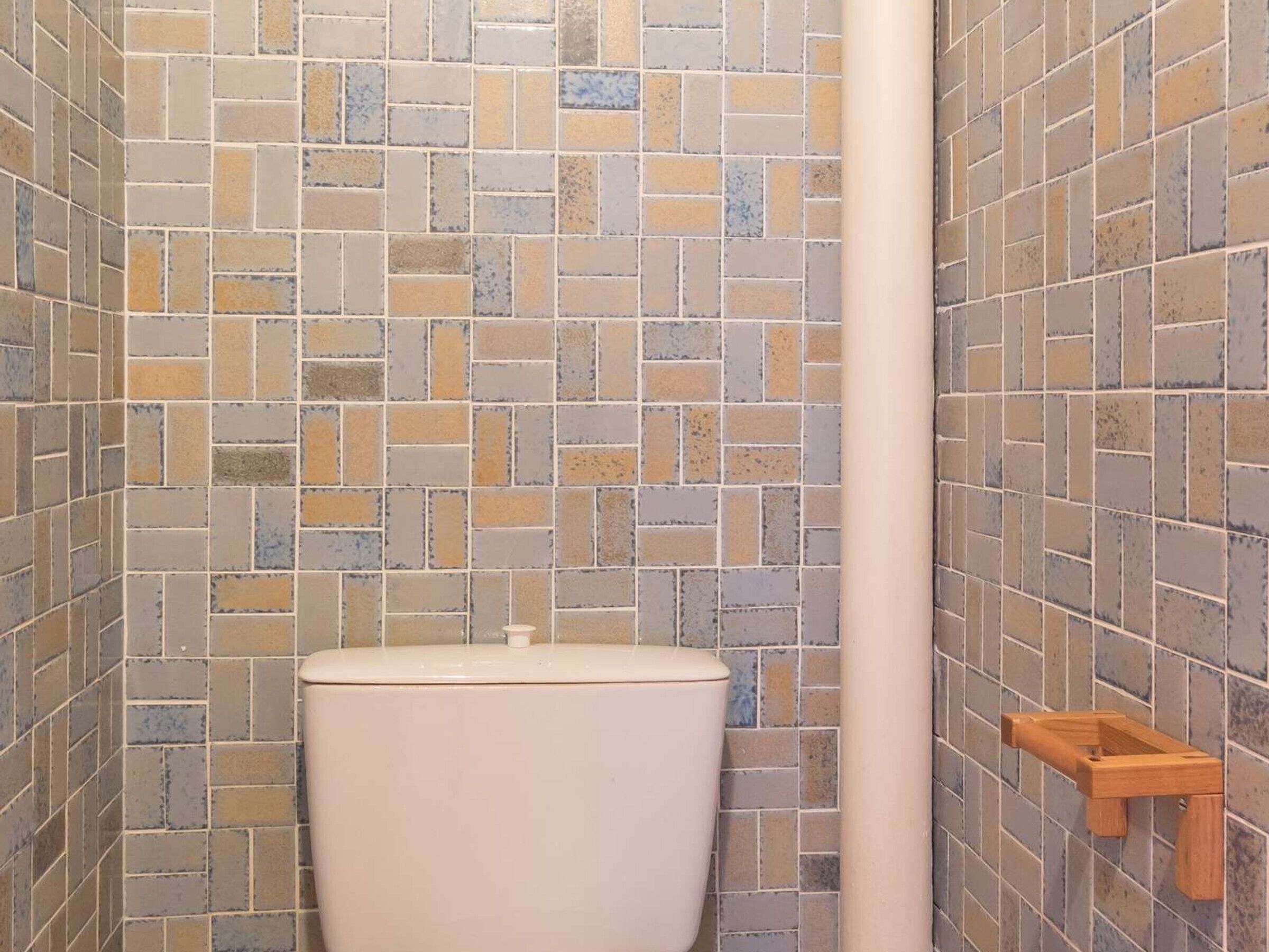 A bathroom with a tiled wall, a toilet, and a wooden shelf.