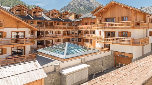 A multi-story wooden building with balconies, a glass-roofed terrace, and a mountain backdrop. - Beautiful 3-room apartment for 7 with balcony, Montgenèvre (Montgenèvre)