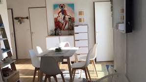 A room with a dining table, chairs, a sofa, a TV, and a painting on the wall. - Appart: T3 Front DE MER -orienté SUD - Terrasse 22 M2-2 Piscines- Parking (lacanau océan)