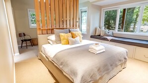 Quarto com cama, um assento junto à janela e um separador de madeira.