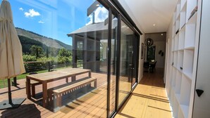 Un intérieur moderne avec une terrasse en bois, un mur de verre donnant sur un jardin et un coin repas avec un banc.