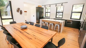 Une cuisine moderne dotée d’un îlot central, d’un coin repas avec une table et des chaises en bois, et de grandes fenêtres qui laissent entrer la lumière naturelle.