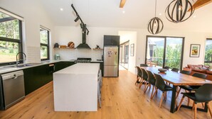 Une cuisine moderne dotée d’un îlot central, d’un coin repas avec des meubles en bois et de grandes fenêtres offrant une vue sur l’extérieur.