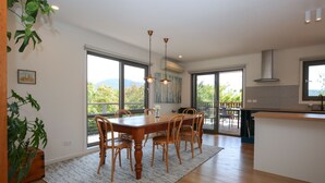 A modern kitchen with a wooden dining table and chairs, large windows, and a view of the outdoors. - BRIGHT VIEWS: Bright (Bright)