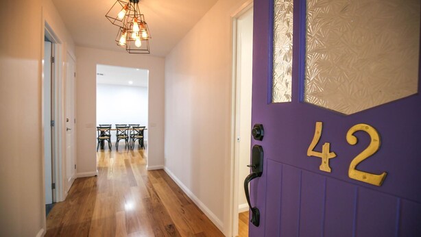 A hallway with wooden flooring, a purple door with the number 42, and a dining area in the background. - BRIGHTER STAYS: Bright (Bright)