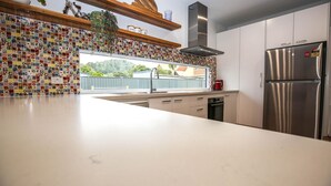 A modern kitchen with a colorful mosaic backsplash, stainless steel appliances, and a window overlooking a residential area. - BRIGHTER STAYS: Bright (Bright)