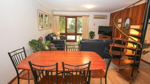 A dining area with a wooden table and chairs, a sofa, and a TV in the background.