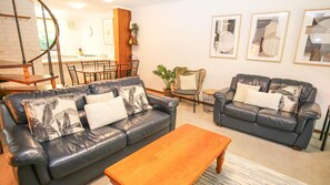 A living room with two leather sofas, a wooden coffee table, and a dining area with a table and chairs.