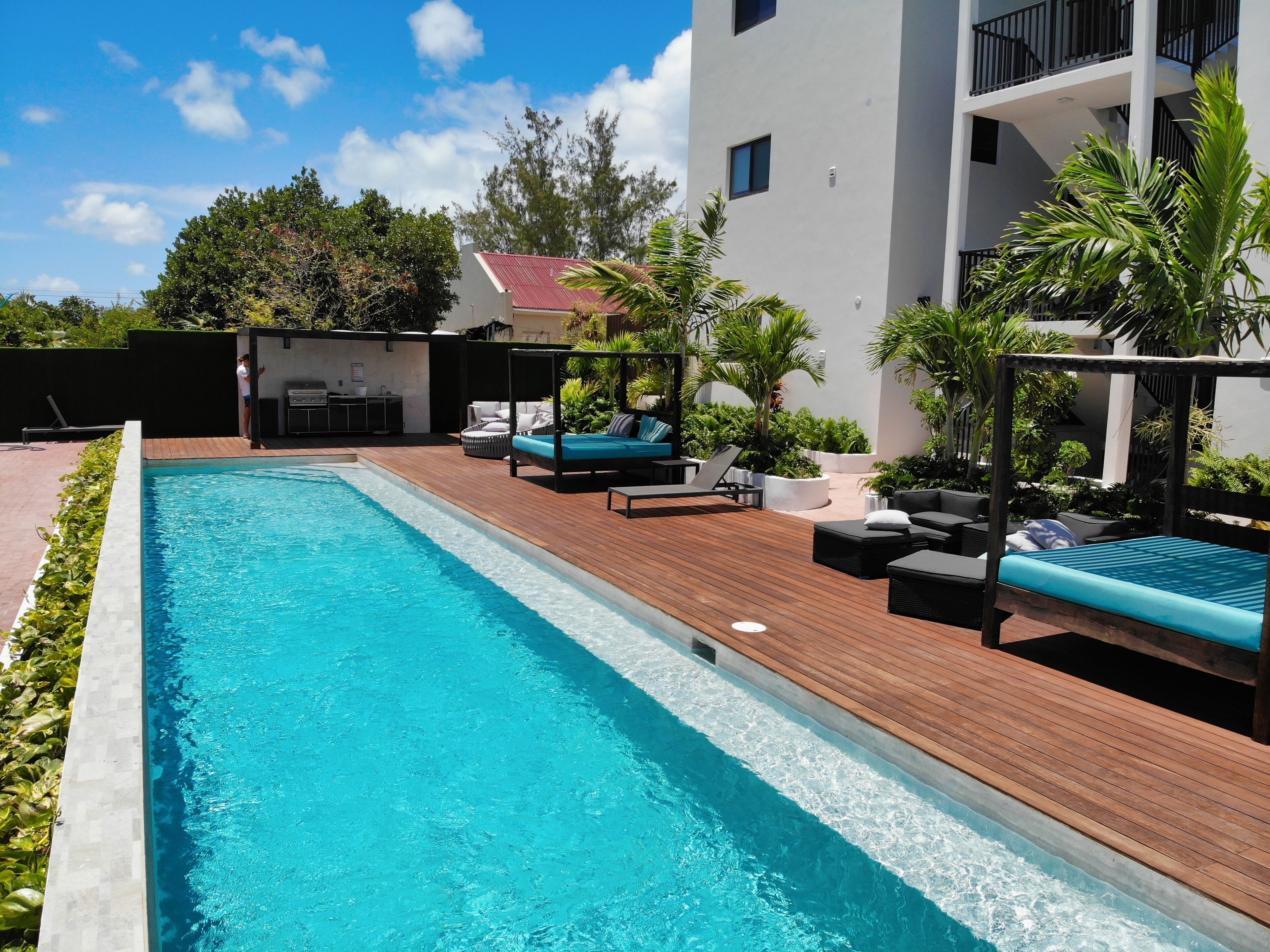 A swimming pool with wooden decking, lounge chairs, and a barbecue area.
