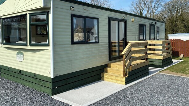 A mobile home with a ramp leading to the entrance, a covered porch, and a small deck area. - Caravan - Sleeps 4 - Pet Friendly - Parking (Newton Stewart)
