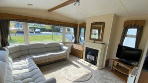 A living room with a sofa, a fireplace, a television, and a view of the outside. - Caravan - Sleeps 4 - Pet Friendly - Parking (Newton Stewart)