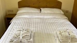 A bed with a wooden headboard, white striped bedding, and two neatly folded towels on the foot of the bed. - Caravan - Sleeps 4 - Pet Friendly - Parking (Newton Stewart)