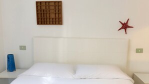 Cama com roupa de cama branca, cabeceira, ventoinha fixada na parede e decoração de estrela-do-mar vermelha.