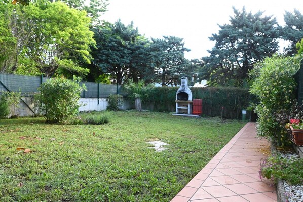 A garden with a paved walkway, a stone structure, and various trees. - N232 - Numana, five-room apartment with garden in a residence with swimming pool (Numana)