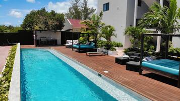 A swimming pool with wooden decking, lounge chairs, and a barbecue area.