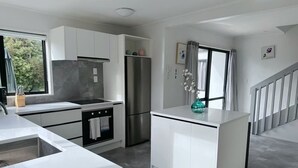 Uma cozinha moderna com armários brancos, uma geladeira de aço inoxidável e uma pequena ilha com um vaso.