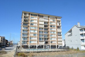 A multi-story residential building with balconies, a swimming pool, and a fenced area. - Comfortable 2 bedroom oceanfront condo with free WiFi, an outdoor pool, and balcony with an amazing ocean view located midtown just steps to the beach! (Ocean City)
